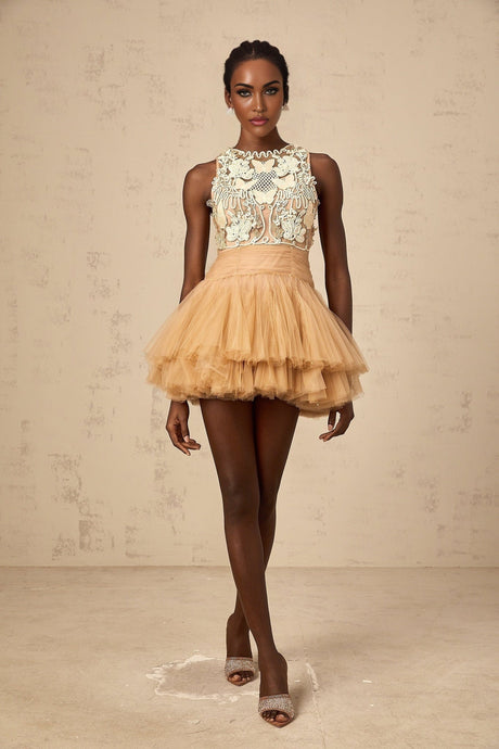 Woman wearing a short khaki dress with sheer tulle overlay and embellished corded lace panels