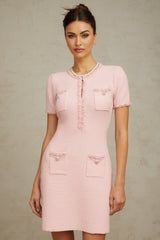 Woman wearing a short pink knitted dress with beaded embellishments standing against a plain background