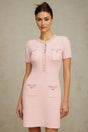 Woman wearing a short pink knitted dress with beaded embellishments standing against a plain background