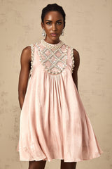 Woman wearing a short pink mini dress with pleated skirt and embellished details