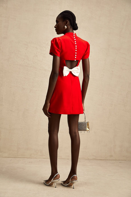 Woman wearing a short red dress with petal sleeves and bow detail featuring a cutout design