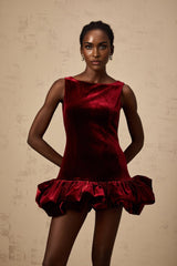 Woman wearing a short red velvet dress with a fitted bodice and flared peplum hem