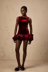 Woman wearing a short red velvet dress with a peplum hem detail standing against a plain background