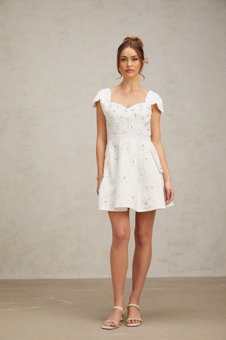Woman wearing a short white dress with flared skirt and embellished details