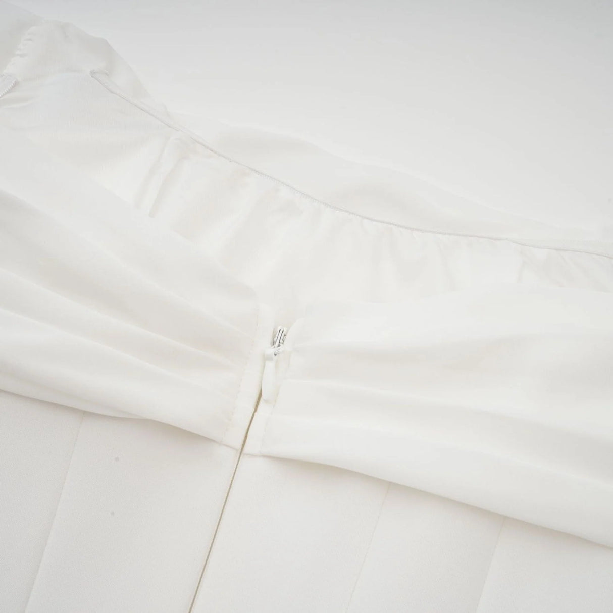 Woman wearing a short white dress with ruched fabric and ribbon design details