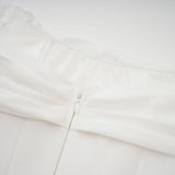 Woman wearing a short white dress with ruched fabric and ribbon design details