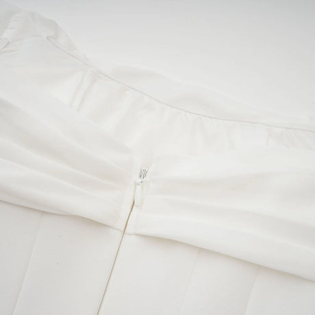 Woman wearing a short white dress with ruched fabric and ribbon design details