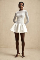 Woman wearing a short white lace dress with panel details and thin straps