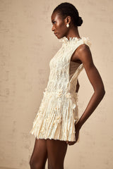 Woman wearing a short white lace dress with semi sheer design and creased texture standing against plain background