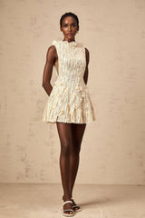 Woman wearing a short white lace dress with semi sheer fabric and creased texture standing in front of a plain background
