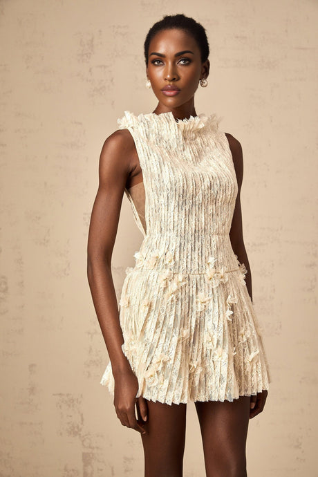 Woman wearing a short white semisheer lace dress with crinkled texture and delicate floral pattern standing against plain background