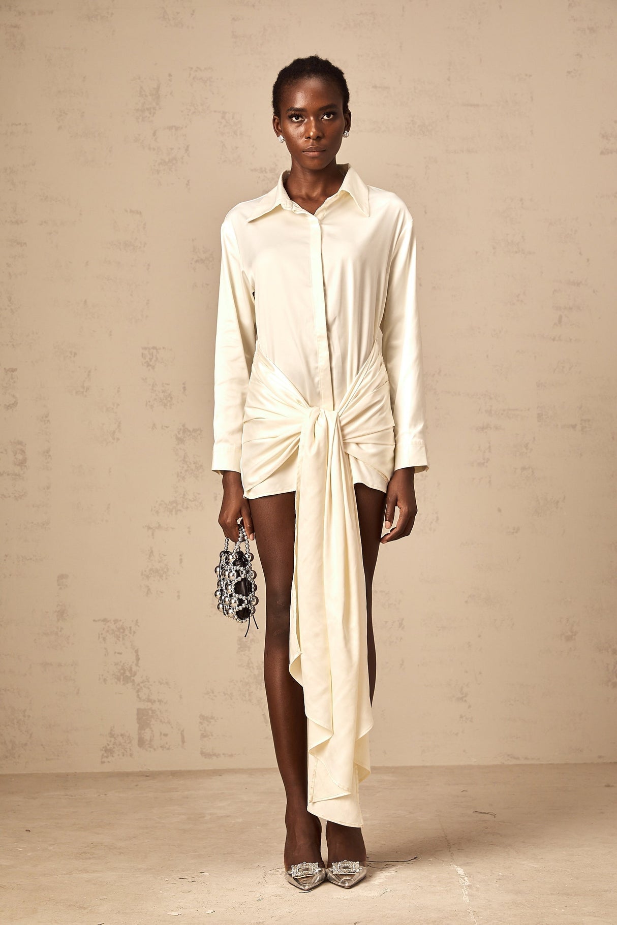 Woman wearing a short white shirt dress with ruched detailing and ribbon accents