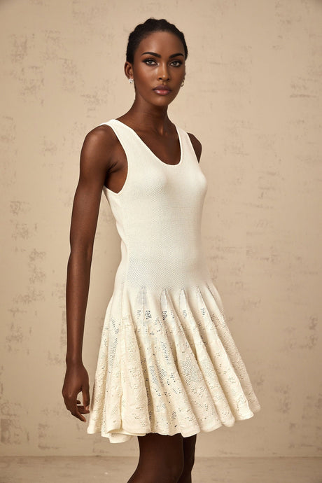 Woman wearing a short white textured knit dress with intricate jacquard pattern standing against plain background
