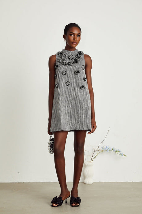 Woman wearing a sleeveless mini dress adorned with colorful faux flowers on a light background