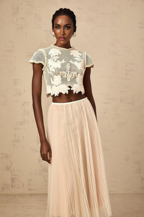 Woman wearing a twopiece outfit in neutral colors with floral applique details top and skirt set