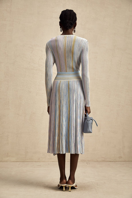 Woman wearing a vertical striped knitted midi dress with alternating colors standing against a plain background