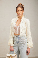 Woman wearing a white cropped jacket with beaded details and ruffle trim