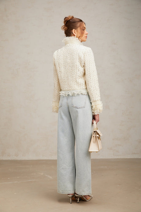 Woman wearing a white cropped jacket with beaded details and ruffle trim