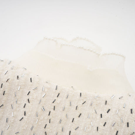 Woman wearing a white cropped jacket with beaded details and ruffle trim
