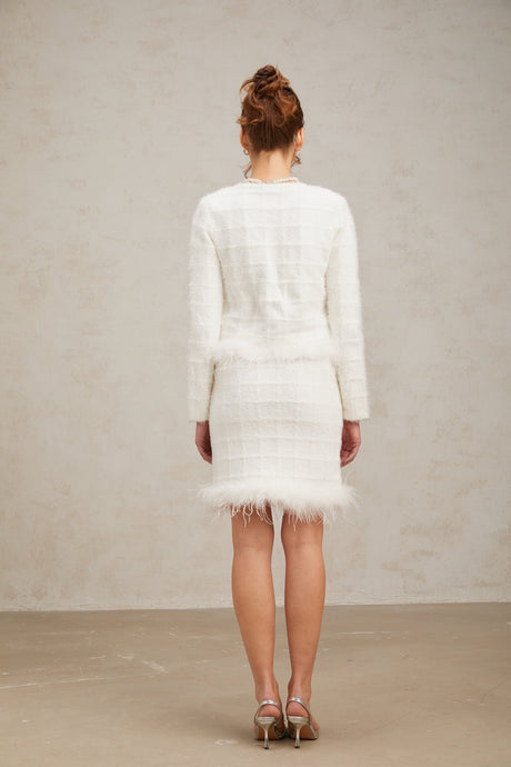 Woman wearing a white feather waffle knit cardigan and matching skirt set standing against a plain background