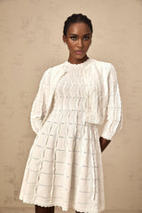 Woman wearing a white knitted cardigan with ruffled details on the sleeves and neckline