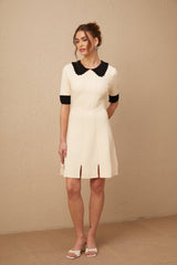 Woman wearing a white knitted mini dress with split hem and short sleeves standing against plain background