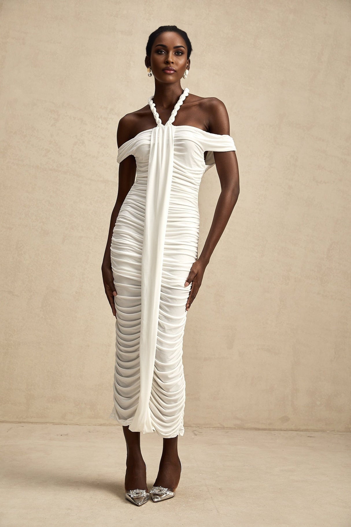 Woman wearing a white midi dress with braided rope details and short sleeves standing against a neutral background