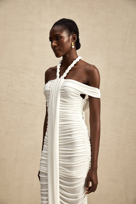 Woman wearing a white midi dress with braided rope details and short sleeves standing against a plain background