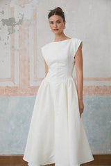 Woman wearing a white midi dress with cap sleeves and open back standing in relaxed pose