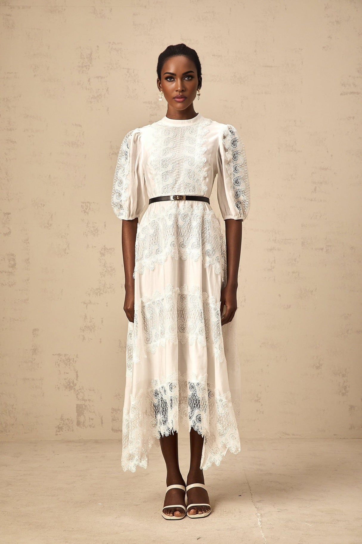 Woman wearing a white midi dress with lace trim panels and a belt at the waist