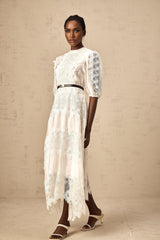 Woman wearing a white midi dress with lace trim panels and a belt at the waist
