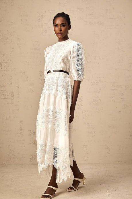 Woman wearing a white midi dress with lace trim panels and a belt at the waist