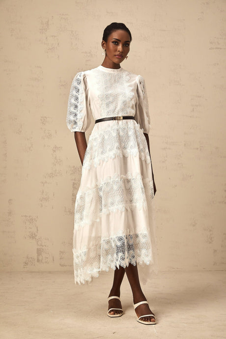 Woman wearing a white midi dress with lace trim panels and a belt at the waist
