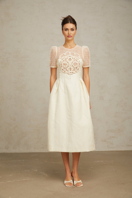 Woman wearing a white midi length dress with braided panelling and sleeveless design