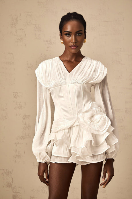 Woman wearing a white mini dress with full pleats and cinched waist detail standing against plain background