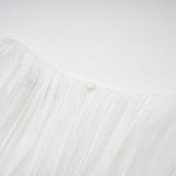 Woman wearing a white mini dress with full pleats and cinched waist detail standing against plain background