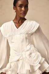 Woman wearing a white pleated mini dress with cinched waist design standing against plain background