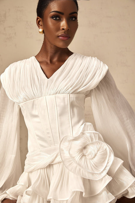 Woman wearing a white pleated mini dress with cinched waist design standing against plain background