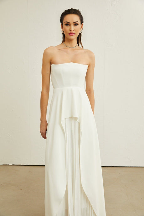 Woman wearing a white pleated off shoulder maxi dress standing in a neutral background