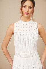 Woman wearing a white sleeveless knitted midi dress with cutout details standing against a plain background
