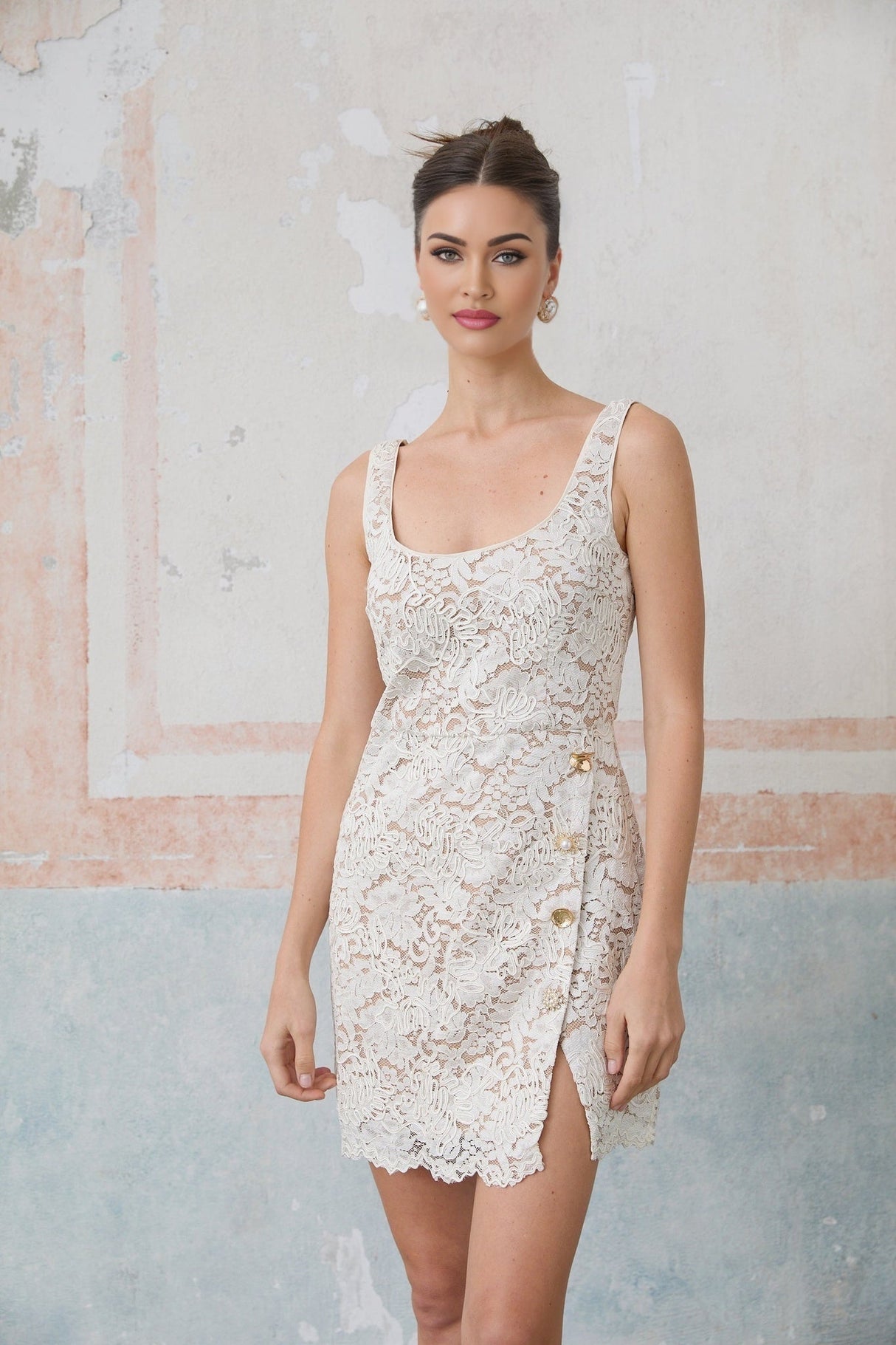 Woman wearing a white sleeveless mini dress made of corded lace with a floral pattern standing against a plain background