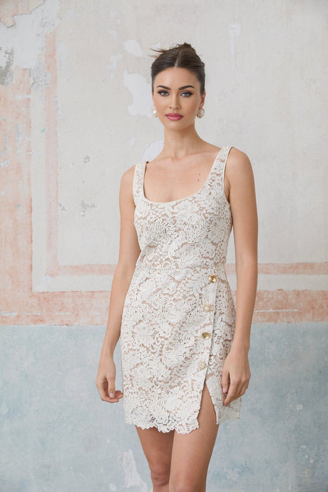 Woman wearing a white sleeveless mini dress made of corded lace with a floral pattern standing against a plain background