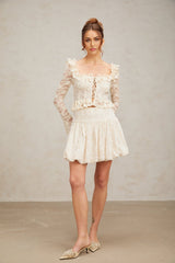 Woman wearing an off white blouse with floral lace pattern and ruffled details