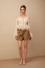 Woman wearing an offshoulder tweed top with feather trim along the neckline and sleeves in a light color