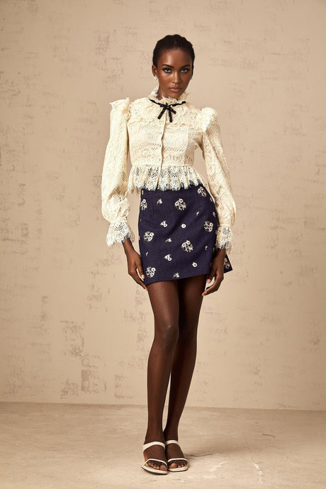 Woman wearing an offwhite blouse with floral lace pattern and a decorative bowknot detail