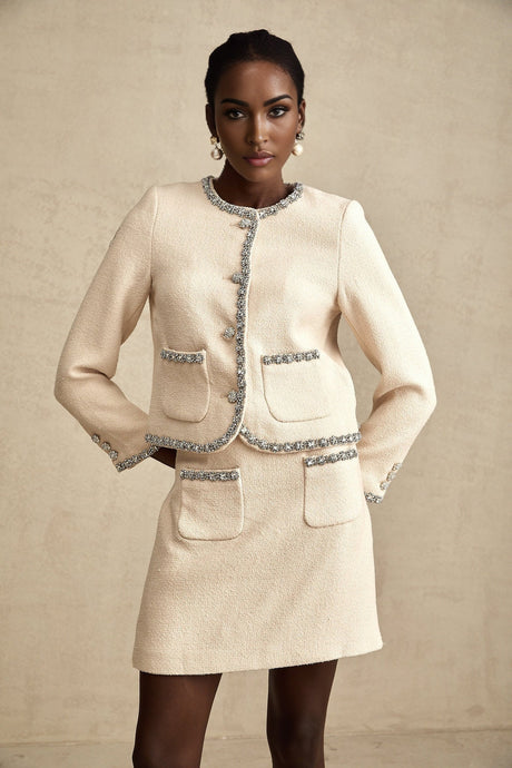 Woman wearing beige tweed cardigan and matching skirt set with crystal embellishments