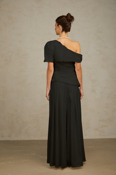 Woman wearing black creased fabric top and matching trousers standing against plain background