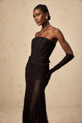 Woman wearing black floral lace corset skirt and gloves set against plain background