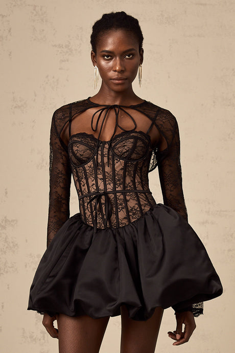Woman wearing black floral lace sleeveless vest over matching dress standing against plain background