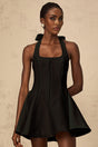 Woman wearing black halterneck mini dress with bow detail at neck